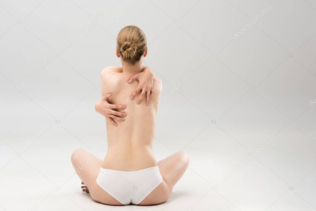 back view of young woman in panties embracing herself while sitting on grey