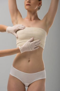 lateks eldivenlerde plastik cerrahın kısmi görünümü ve gri üzerinde izole edilmiş meme bandajında hasta