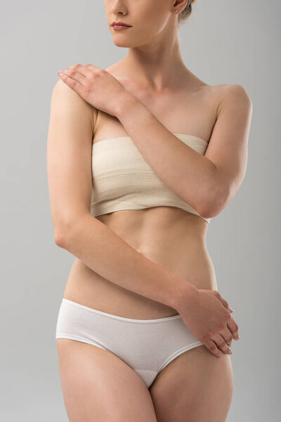 cropped view of woman in panties with breast bandage isolated on grey