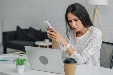 güzel ve esmer kadın akıllı telefon tutan ve dizüstü ekran bakarak