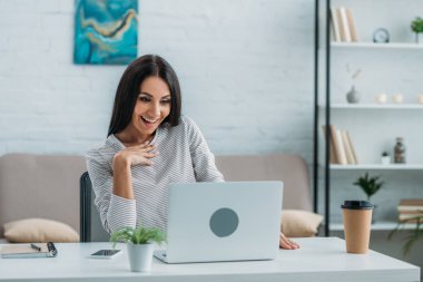 esmer ve çekici kadın dizüstü bilgisayar bakarak ve gülümseyerek 