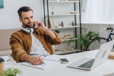 kulaklıklı yakışıklı adam dizüstü bilgisayar ekranına bakıyor ve kalem tutuyor 
