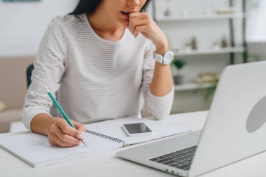 cropped view of woman writing in notebook with pencil  clipart