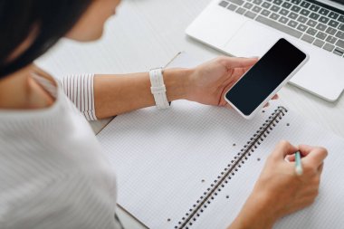 dizüstü bilgisayara yazı yazan ve akıllı telefon tutan kadının kırpılmış görünümü 
