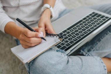 cropped view of woman writing in notebook and holding laptop  clipart