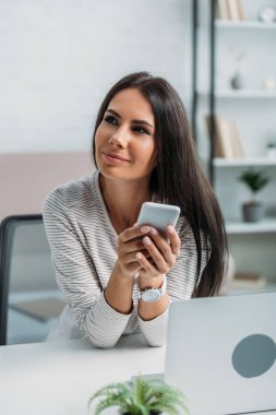 çekici ve esmer kadın akıllı telefon tutarak ve uzağa bakıyor 