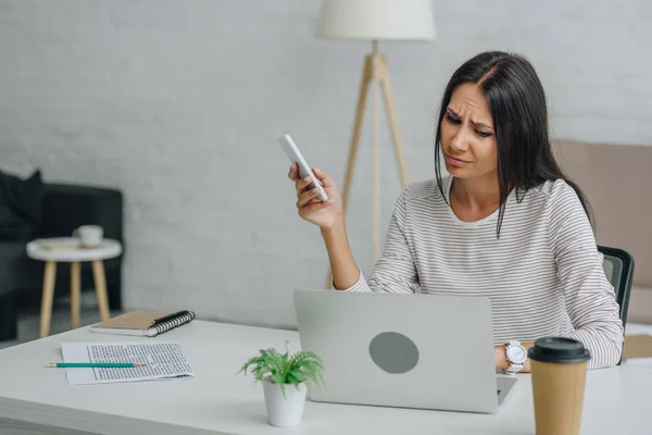 Chateado Mulher Bonita Morena Segurando Smartphone Olhando Para Tela Laptop — Fotografia de Stock