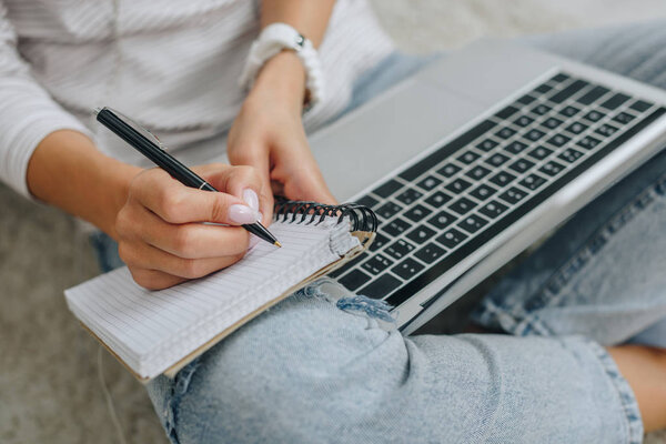 cropped view of woman writing in notebook and holding laptop 