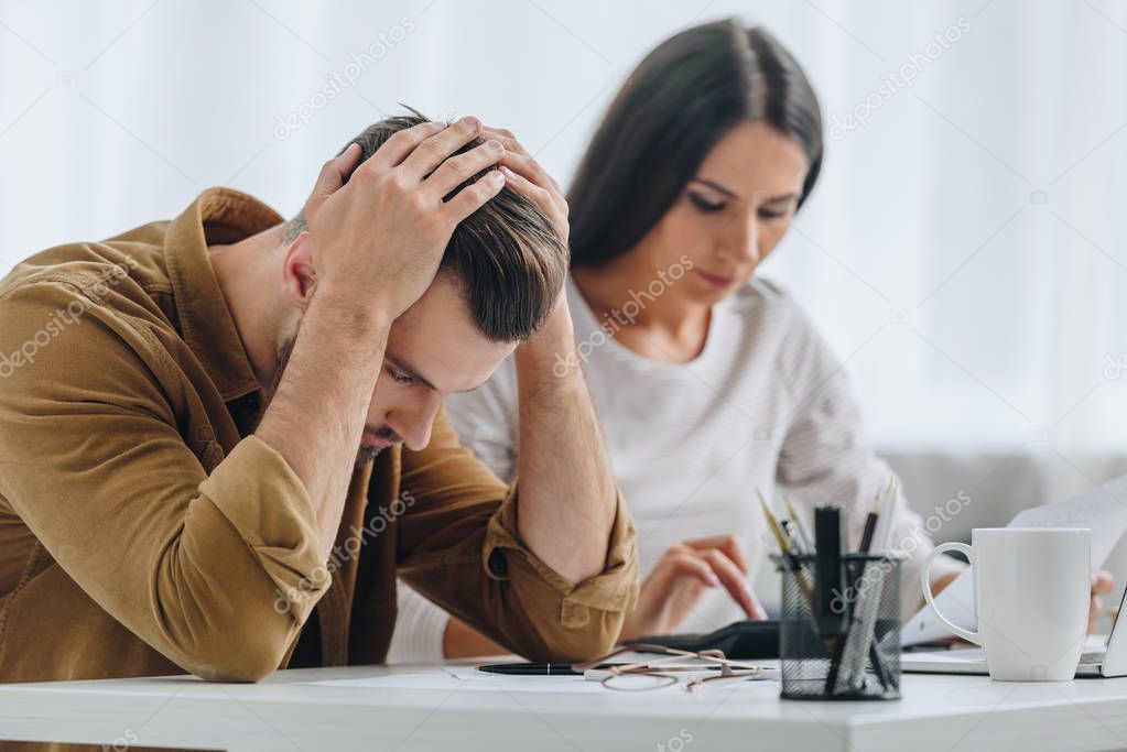 sad and handsome man holding head and attractive woman using calculator 