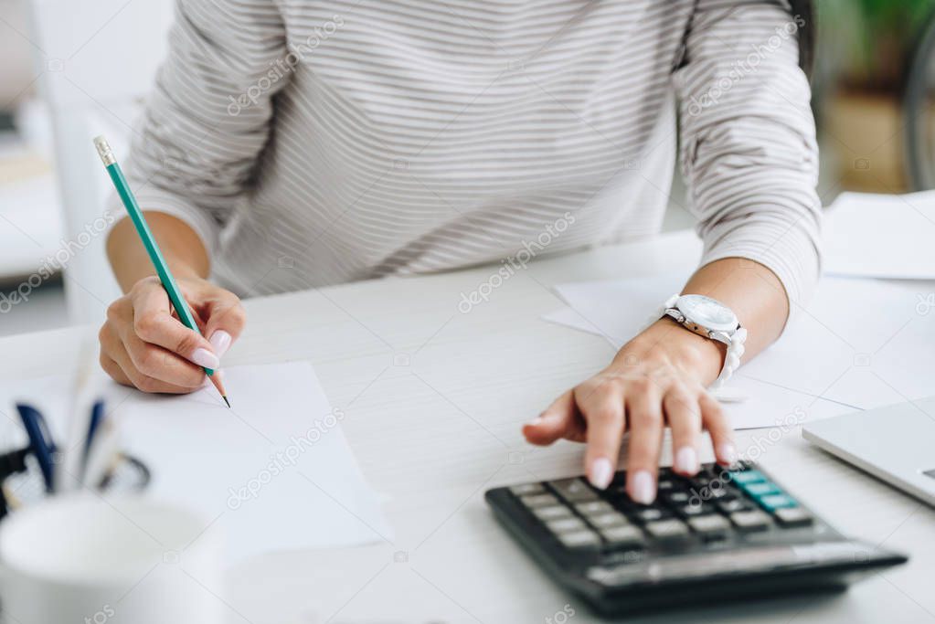 cropped view of woman using calculator and writing with pencil 