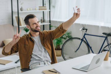 yakışıklı ve mutlu adam gülümseyerek, selfie alarak ve barış işareti gösteren 
