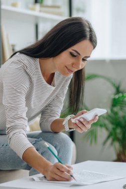 akıllı telefon kullanarak çekici ve esmer kadın ve kalem ile yazma 