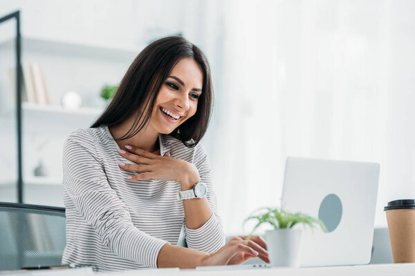 happy and attractive woman smiling and looking at screen of laptop 