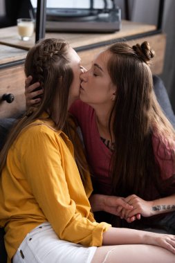 oturma odasında kanepede otururken iki Lezbiyenler öpüşme ve eller tutarak