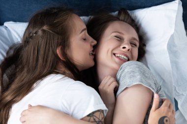 yatakta yatarken kucaklayan iki gülümseyen lezbiyenler