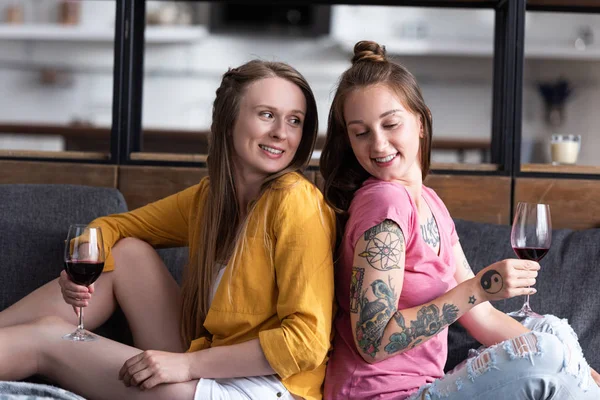 Dos Lesbianas Sonrientes Sosteniendo Copas Vino Mientras Están Sentadas Sofá —  Fotos de Stock