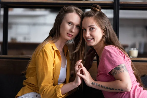 Dos Lesbianas Sonrientes Tocando Las Manos Mirando Cámara Sala Estar —  Fotos de Stock