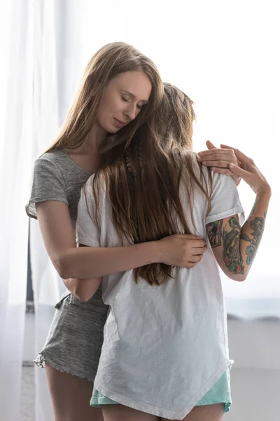 两个微笑的女同性恋在T恤拥抱在卧室 — 图库照片