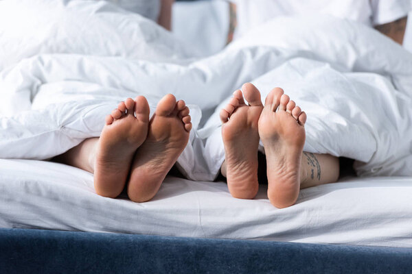 partial view of two barefoot lesbians lying under blanket