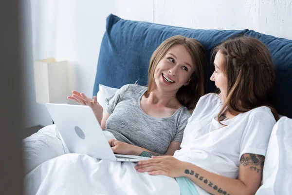 Dos Lesbianas Sonrientes Mirándose Mientras Usan Portátil Cama Por Mañana — Foto de Stock