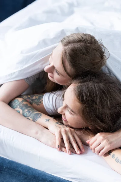 Twee Glimlachende Lesbiennes Omarmen Terwijl Liggend Onder Deken Bed — Stockfoto