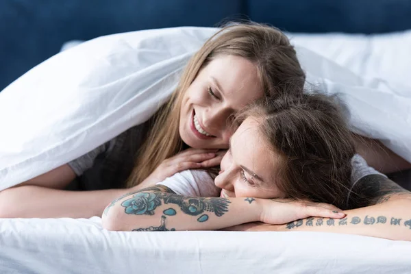 Twee Glimlachende Lesbiennes Omarmen Terwijl Liggend Onder Deken Bed — Stockfoto