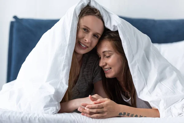 Duas Lésbicas Felizes Mãos Dadas Enquanto Deitado Debaixo Cobertor Cama — Fotografia de Stock