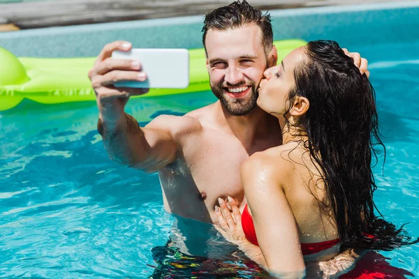 Enfoque Selectivo Mujer Besar Mejilla Hombre Feliz Tomando Selfie Piscina —  Fotos de Stock