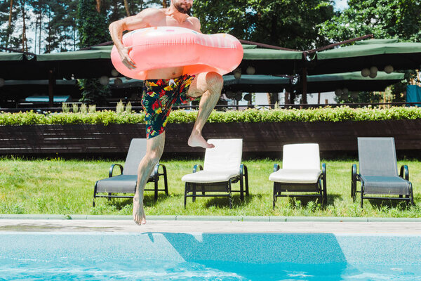 cropped view of bearded man with barefoot jumping in water while holding inflatable ring