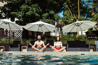 güzel kadın ve yakışıklı adam yüzme havuzu yakınında meditasyon  