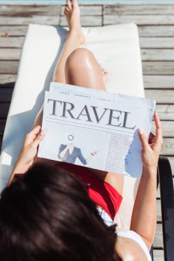 şezlongda otururken seyahat gazetesi okuyan genç kadının üst görünümü 