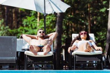 handsome man and beautiful woman in sunglasses lying on deck chairs  clipart