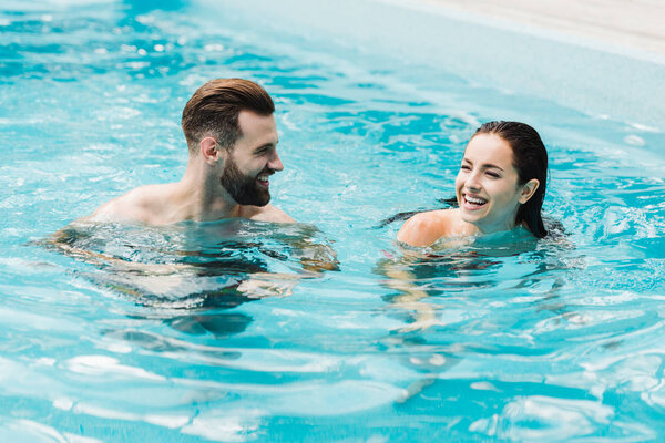 handsome bearded man looking at attractive woman in swimming pool 