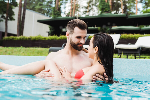 selective focus of bearded man looking at young woman smiling in swimming pool 