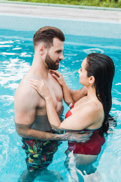 brunette woman hugging handsome bearded man in swimming pool 