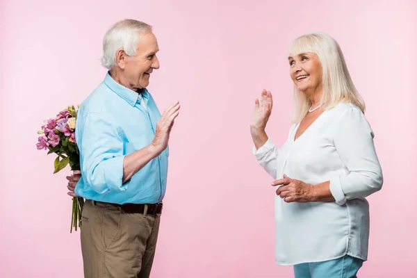 Fröhlicher Älterer Mann Winkt Frau Und Hält Blumenstrauß Auf Rosa — Stockfoto