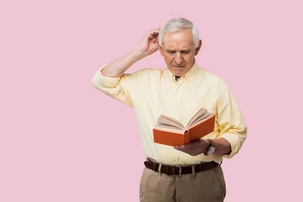 沉思的资深男子触摸灰色的头发和阅读书孤立在粉红色 — 图库照片