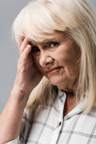 close up of tired and s sad tired woman touching head and looking at camera isolated on grey 
