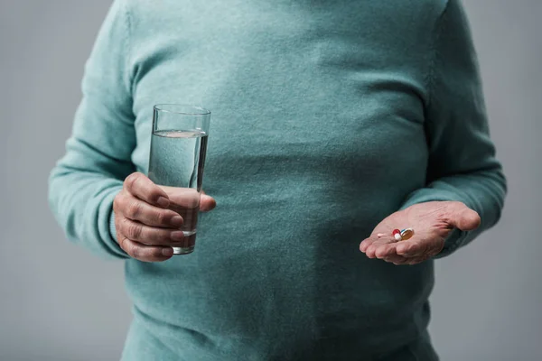 Beskuren Över Pensionerade Man Holding Piller Och Glas Vatten Isolerade — Gratis stockfoto