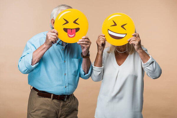 KYIV, UKRAINE - JUNE 14, 2019: retired couple covering faces with yellow happy smileys isolated on beige 