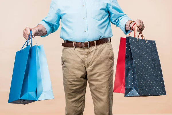 裁剪视图退休男子微笑拿着购物袋孤立米色 — 图库照片