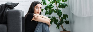 evde yerde otururken ve kameraya bakarken depresyon dan muzdarip sinirli genç kadının panoramik çekim