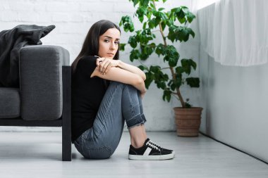 depressed young woman sitting on floor at home and looking at camera clipart