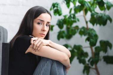 yerde otururken ve kameraya bakarken depresyon dan muzdarip sinirli genç kadın