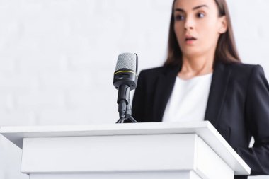selective focus of scared young lecturer, suffering from fear of public speaking, standing near microphone on podium tribune clipart