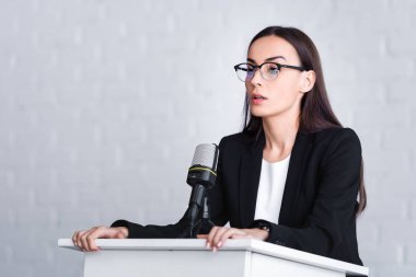 nervous lecturer in glasses standing on podium tribune and looking away clipart