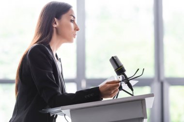 konferans salonunda podyum tribünü üzerinde dururken gözlük tutan ciddi öğretim görevlisi