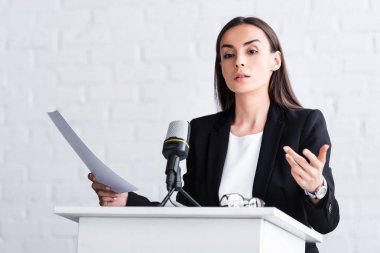 podyum tribününde mikrofona konuşurken kendinden emin öğretim görevlisi gesturing