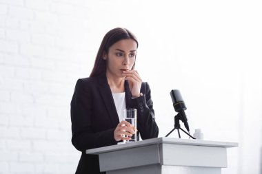 young lecturer suffering from speech anxiety standing on podium tribune with glass of water clipart