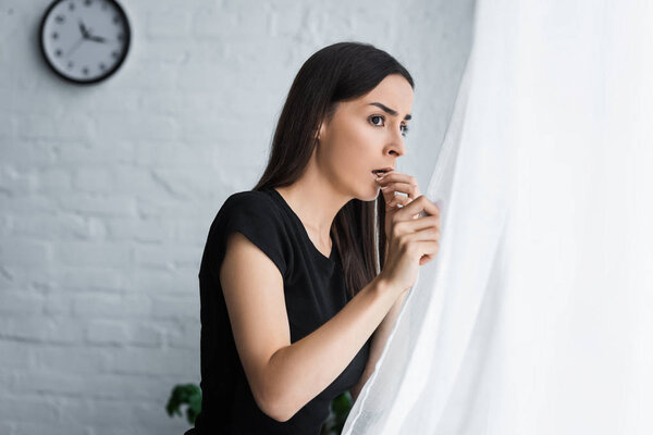 frightened girl looking out window while suffering from panic attack at home